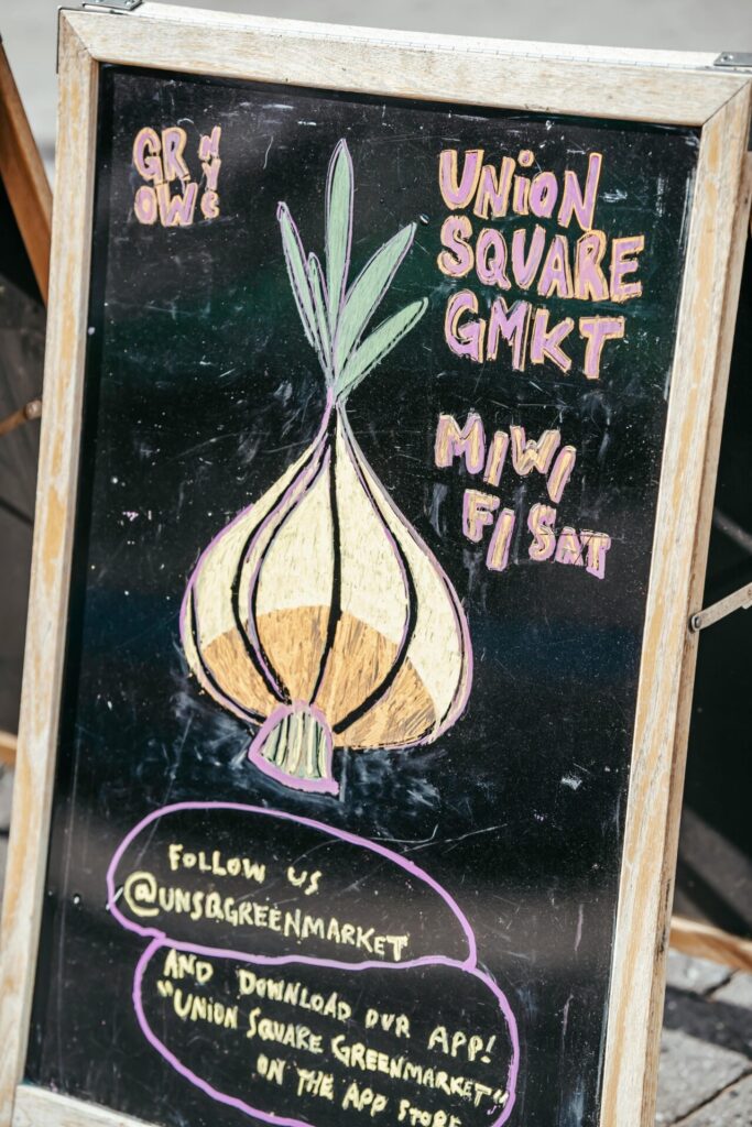Chalkboard with colorful onion and local market invitation placed in street in daytime