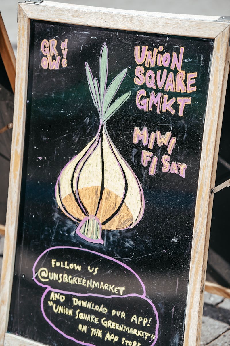 Chalkboard with colorful onion and local market invitation placed in street in daytime