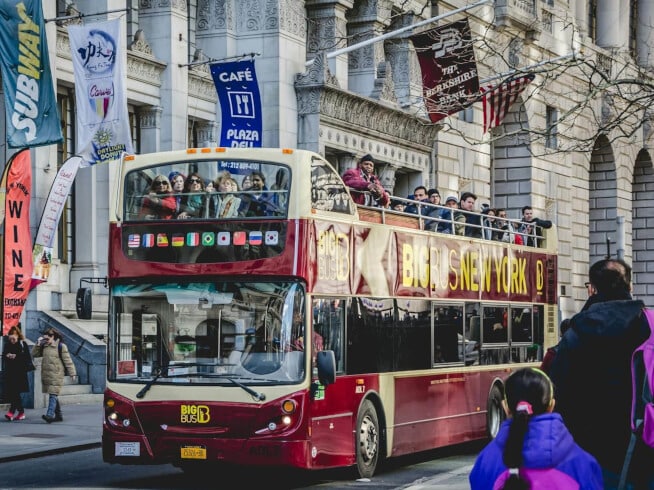 Double-decker bus with tourists sightseeing in downtown New York City on a sunny day.